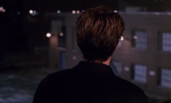 Movie still from “Crash” (1996), directed by David Cronenberg – A man standing in front of a building at night; Close Up shot, Over the shoulder angle