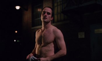 Movie still from “Crash” (1996), directed by David Cronenberg – A shirtless man standing in front of a brick building; Medium shot, Low angle