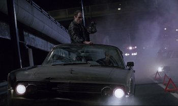 Movie still from “Crash” (1996), directed by David Cronenberg – A man on the hood of a car at night; Wide shot, Low angle