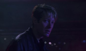 Movie still from “Crash” (1996), directed by David Cronenberg – A young man is standing in a dark room; Close Up shot, Low angle