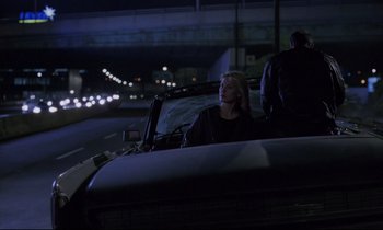 Movie still from “Crash” (1996), directed by David Cronenberg – A woman sitting in the driver's seat of a car at night; Wide shot, Over the shoulder angle