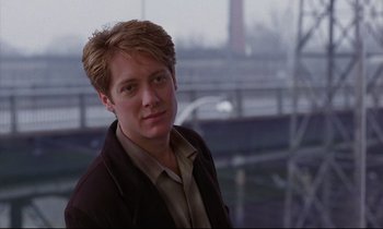 Movie still from “Crash” (1996), directed by David Cronenberg – A young man in a brown jacket is posing for a picture; Close Up shot, Over the shoulder angle