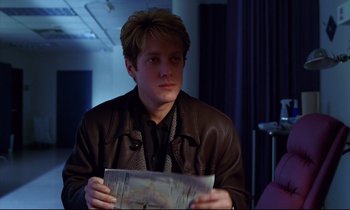 Movie still from “Crash” (1996), directed by David Cronenberg – A man in a brown jacket is holding a newspaper; Close Up shot, Over the shoulder angle
