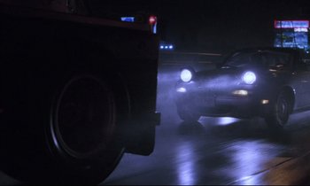 Movie still from “Crash” (1996), directed by David Cronenberg – Two cars driving down a street at night with headlights on; Wide shot, Low angle