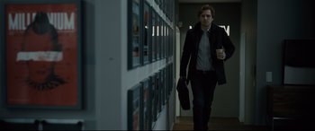 Movie still from “The Girl in the Spider's Web” (2018), directed by Fede Alvarez – A man walking down a hallway holding a bag of coffee; Medium shot, Over the shoulder angle