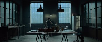Movie still from “The Girl in the Spider's Web” (2018), directed by Fede Alvarez – A person standing in a room with a table; Wide shot, Low angle