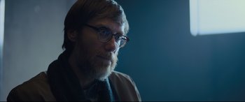 Movie still from “The Girl in the Spider's Web” (2018), directed by Fede Alvarez – A man with a beard wearing glasses and a tie; Close Up shot, Over the shoulder angle