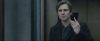 Movie still from “The Girl in the Spider's Web” (2018), directed by Fede Alvarez – A man in a black coat standing in front of a window; Close Up shot, Low angle