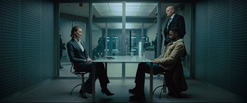Movie still from “The Girl in the Spider's Web” (2018), directed by Fede Alvarez – A group of people sitting at a table in an office; Wide shot, Low angle