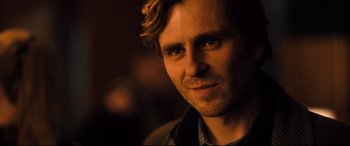 Movie still from “The Girl in the Spider's Web” (2018), directed by Fede Alvarez – A man's face in a dimly - lit room; Close Up shot, Over the shoulder angle