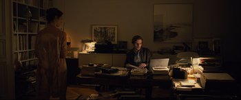 Movie still from “The Girl in the Spider's Web” (2018), directed by Fede Alvarez – A man sitting at a desk with a laptop; Wide shot, High angle