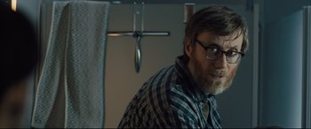 Movie still from “The Girl in the Spider's Web” (2018), directed by Fede Alvarez – A man with a beard wearing glasses and a plaid shirt; Close Up shot, Over the shoulder angle