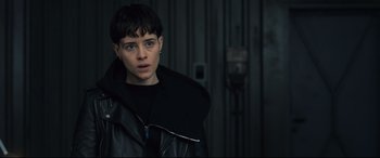 Movie still from “The Girl in the Spider's Web” (2018), directed by Fede Alvarez – A woman in a black leather jacket standing next to a wall; Close Up shot, Over the shoulder angle