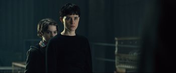Movie still from “The Girl in the Spider's Web” (2018), directed by Fede Alvarez – A woman standing next to another woman in a dark room; Medium shot, Over the shoulder angle