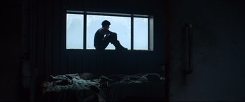 Movie still from “The Girl in the Spider's Web” (2018), directed by Fede Alvarez – A man sitting on a window sill looking out a window; Wide shot, Low angle