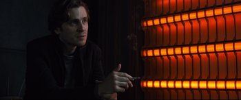 Movie still from “The Girl in the Spider's Web” (2018), directed by Fede Alvarez – A man smoking a cigarette in front of an illuminated wall; Close Up shot, Over the shoulder angle