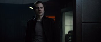 Movie still from “The Girl in the Spider's Web” (2018), directed by Fede Alvarez – A man standing in a dark room looking at the camera; Medium shot, Over the shoulder angle