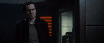 Movie still from “The Girl in the Spider's Web” (2018), directed by Fede Alvarez – A man standing in front of a mirror in a dark room; Medium shot, Over the shoulder angle