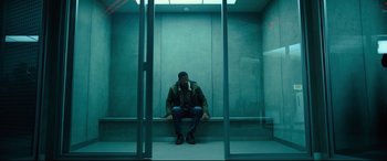 Movie still from “The Girl in the Spider's Web” (2018), directed by Fede Alvarez – A man sitting on a bench in an elevator; Wide shot, Low angle