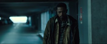 Movie still from “The Girl in the Spider's Web” (2018), directed by Fede Alvarez – A man wearing a jacket and glasses in a dark room; Medium shot, Over the shoulder angle