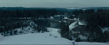 Movie still from “The Girl in the Spider's Web” (2018), directed by Fede Alvarez – An aerial view of a snowy landscape with trees and buildings; Extreme Wide shot, High angle