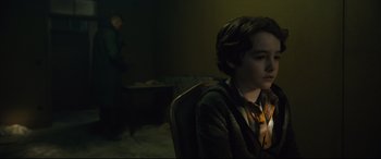 Movie still from “The Girl in the Spider's Web” (2018), directed by Fede Alvarez – A young man sitting in a chair in a dark room; Medium shot, Over the shoulder angle