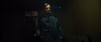 Movie still from “The Girl in the Spider's Web” (2018), directed by Fede Alvarez – A man in a black coat holding a gun; Medium shot, Low angle