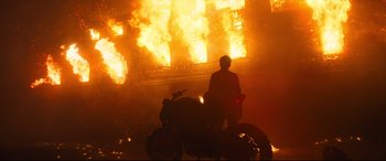Movie still from “The Girl in the Spider's Web” (2018), directed by Fede Alvarez – A person on a motorcycle in front of a building on fire; Wide shot, Low angle