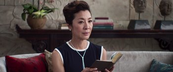 Movie still from “Crazy Rich Asians” (2018), directed by Jon M. Chu – A woman sitting on a couch holding an open book; Close Up shot, Over the shoulder angle