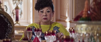 Movie still from “Crazy Rich Asians” (2018), directed by Jon M. Chu – A woman sitting at a dinner table looking at the camera; Close Up shot, Over the shoulder angle