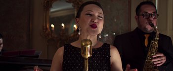Movie still from “Crazy Rich Asians” (2018), directed by Jon M. Chu – A woman in a black dress holding a gold microphone; Close Up shot, Low angle