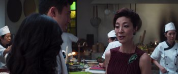 Movie still from “Crazy Rich Asians” (2018), directed by Jon M. Chu – A group of people standing around a table with food on top of it; Close Up shot, Over the shoulder angle