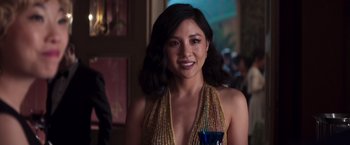 Movie still from “Crazy Rich Asians” (2018), directed by Jon M. Chu – A woman in a gold dress smiling for the camera; Close Up shot, Over the shoulder angle