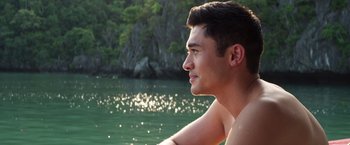 Movie still from “Crazy Rich Asians” (2018), directed by Jon M. Chu – A man sitting on a boat in a body of water; Close Up shot, High angle
