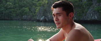 Movie still from “Crazy Rich Asians” (2018), directed by Jon M. Chu – A man sitting on a boat in a body of water; Close Up shot, Over the shoulder angle