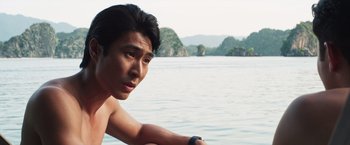 Movie still from “Crazy Rich Asians” (2018), directed by Jon M. Chu – A man sitting on the side of a body of water; Close Up shot, Low angle