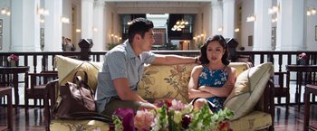 Movie still from “Crazy Rich Asians” (2018), directed by Jon M. Chu – A man and a woman are sitting on a couch; Medium shot, Over the shoulder angle