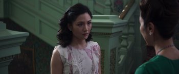 Movie still from “Crazy Rich Asians” (2018), directed by Jon M. Chu – A woman in a white and pink dress standing in front of a staircase; Close Up shot, Over the shoulder angle