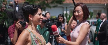 Movie still from “Crazy Rich Asians” (2018), directed by Jon M. Chu – A woman is being interviewed by a reporter; Close Up shot, Over the shoulder angle