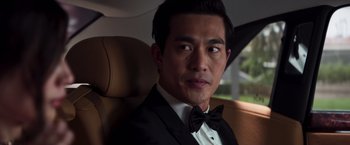Movie still from “Crazy Rich Asians” (2018), directed by Jon M. Chu – A person wearing a suit in a car; Close Up shot, Over the shoulder angle