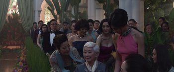 Movie still from “Crazy Rich Asians” (2018), directed by Jon M. Chu – A group of people standing around a woman; Medium shot, Over the shoulder angle