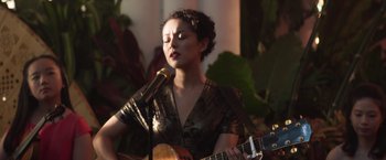 Movie still from “Crazy Rich Asians” (2018), directed by Jon M. Chu – A woman holding a microphone while holding a guitar; Medium shot, Low angle