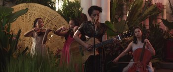Movie still from “Crazy Rich Asians” (2018), directed by Jon M. Chu – A woman playing a guitar while another woman plays an instrument; Medium shot, Low angle