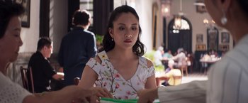 Movie still from “Crazy Rich Asians” (2018), directed by Jon M. Chu – A woman sitting at a table in front of other people; Medium shot, Over the shoulder angle