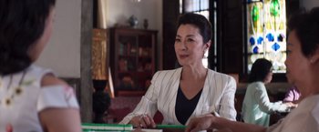 Movie still from “Crazy Rich Asians” (2018), directed by Jon M. Chu – A woman sitting at a table with a pen in her hand; Medium shot, Over the shoulder angle