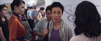 Movie still from “Crazy Rich Asians” (2018), directed by Jon M. Chu – Two women are standing on a crowded airplane; Close Up shot, Over the shoulder angle
