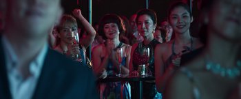 Movie still from “Crazy Rich Asians” (2018), directed by Jon M. Chu – A group of women sitting at a table holding drinks; Medium shot, Over the shoulder angle