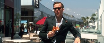 Movie still from “Crazy, Stupid, Love.” (2011), directed by Glenn Ficarra – A man in a suit and sunglasses eating a slice of pizza; Medium shot, Over the shoulder angle