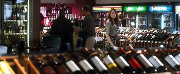 Movie still from “Crazy, Stupid, Love.” (2011), directed by Glenn Ficarra – A woman standing in front of bottles of wine in a wine shop; Wide shot, Over the shoulder angle