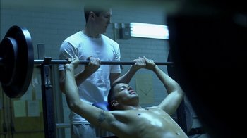 Movie still from “Crazy/Beautiful” (2001), directed by John Stockwell – A man lifting a barbell above his head while another man watches; Medium shot, Over the shoulder angle